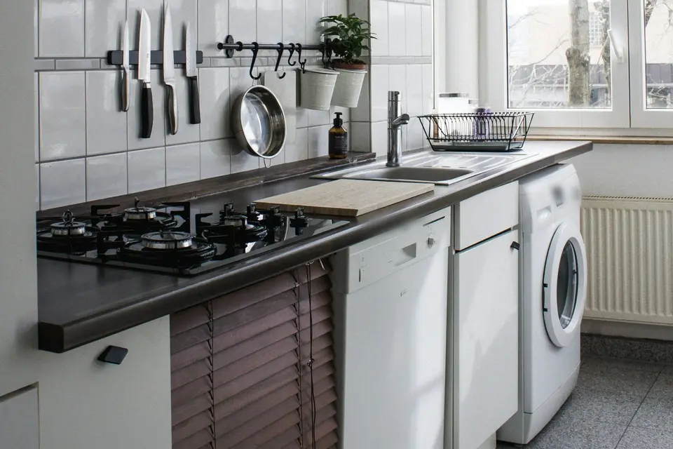 Een keuken met een vaatwasser en een wasmachine onder het aanrecht, met daglicht door het raam