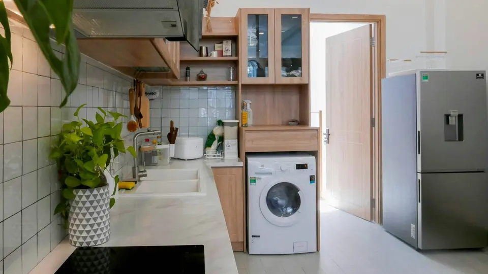 Een witte wasmachine in een lichte keuken met planten en houten kastjes
