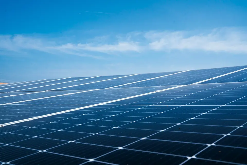 Rijen zonnepanelen op een dak onder een blauwe lucht, rond het middaguur